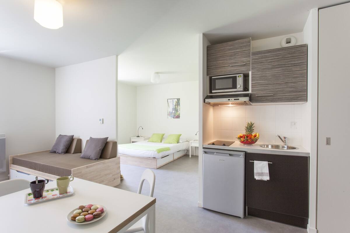 A compact, modern apartment with a kitchenette, a dining area, and a bedroom.