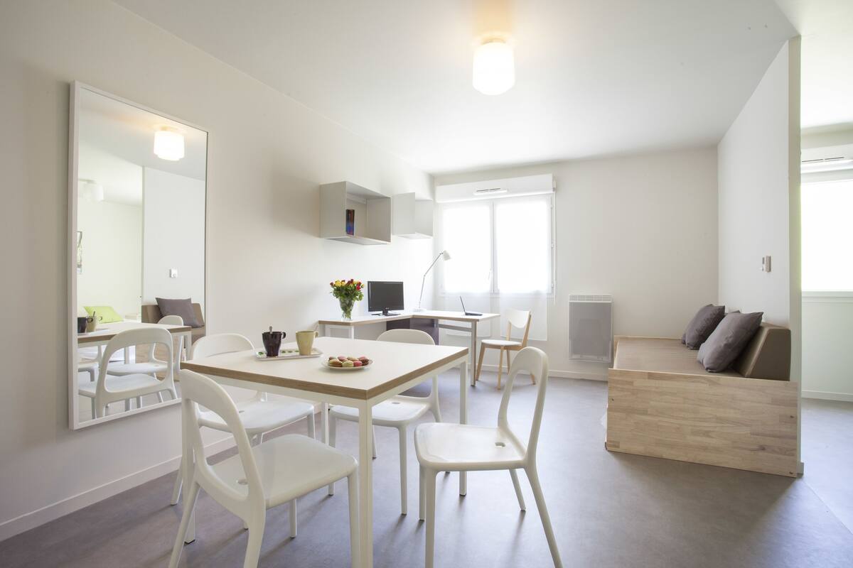 A modern, well-lit room with a dining table, chairs, a sofa, and a TV.