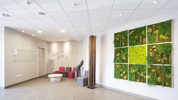 Un área de espera moderna con mostrador de recepción, asientos y un amplio jardín vertical.