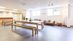 Una habitación amplia con una gran mesa de madera, bancos, un sofá y un pequeño taburete.