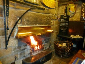 A stone fireplace with a visible fire, a blackboard menu listing food items, and a wicker basket on the floor. - Blacksmiths Arms Inn (Scarborough)