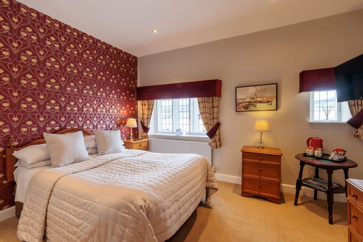 Quarto com cama grande, cômoda, mesa de cabeceira e janela com cortinas.