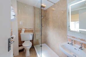 A modern bathroom with a glass-enclosed shower, a toilet, and a sink with two faucets.