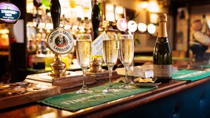 Una barra con tres copas de champán, una botella de vino y un grifo de cerveza que dice 'STOWFORD PRESS'.