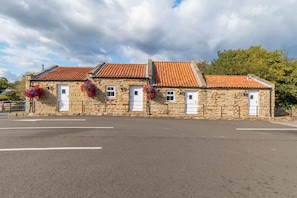 A stone building with a red-tiled roof, multiple doors, and hanging flower baskets.