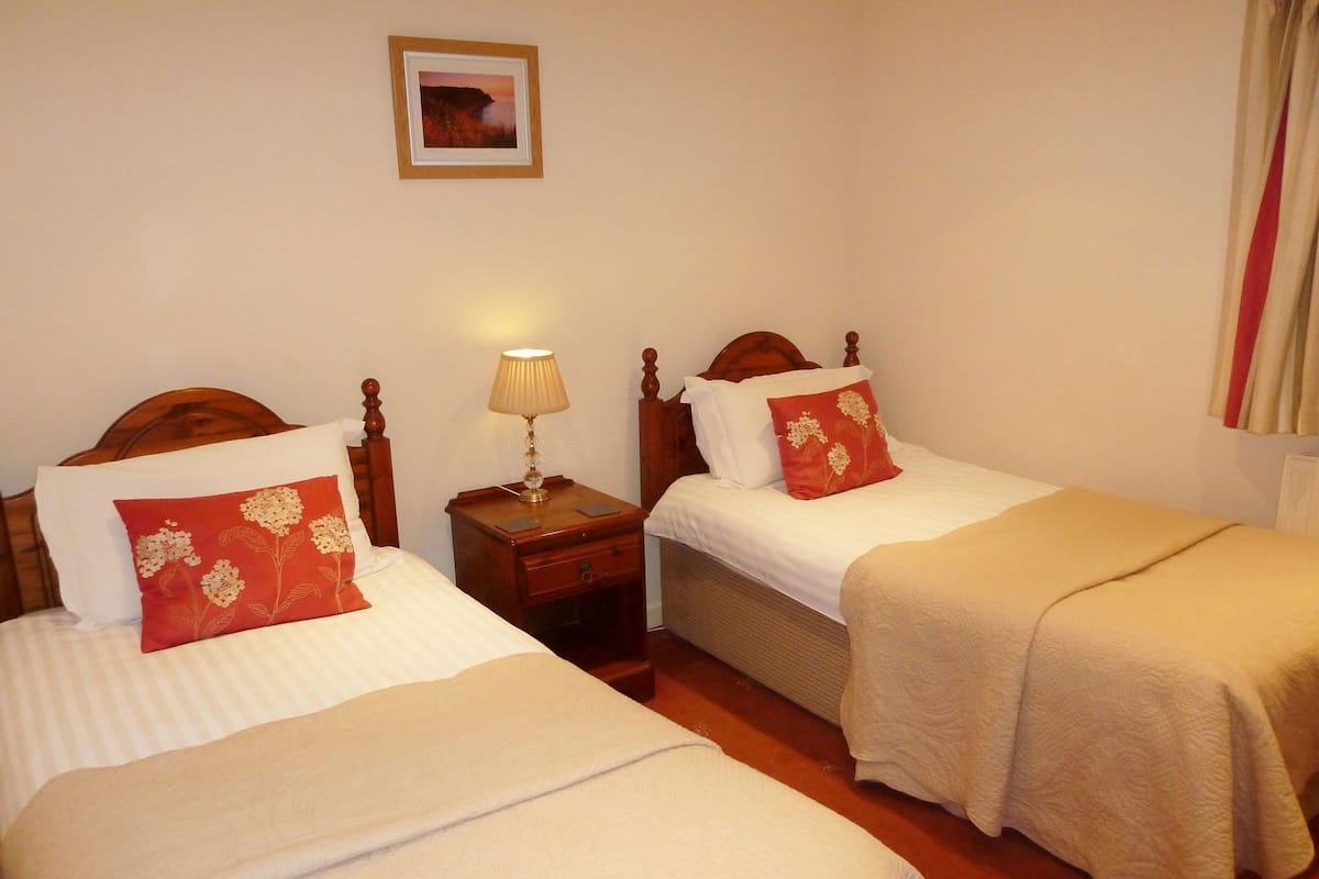 Quarto de hotel com duas camas, uma mesa de cabeceira com abajur e um quadro na parede.