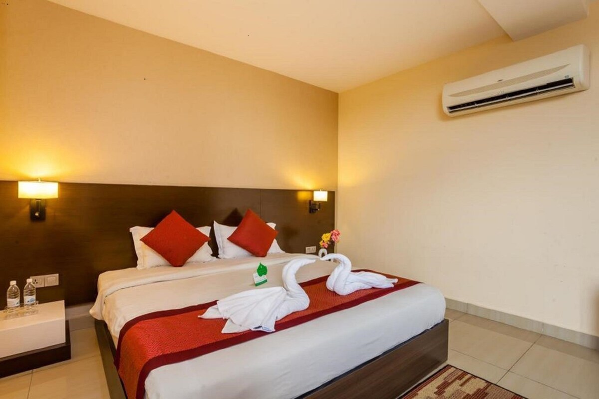 A hotel room with a bed, pillows, a nightstand, a water bottle, a towel, and an air conditioning unit.