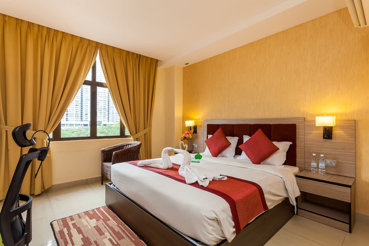A hotel room with a bed, two bedside lamps, a nightstand, a window with curtains, and a view of a building outside.