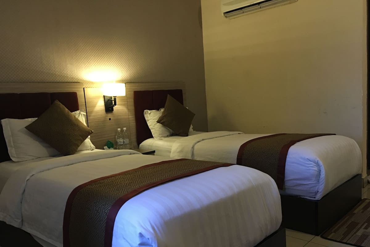 A hotel room with two beds, a nightstand with a lamp, and an air conditioning unit on the wall.