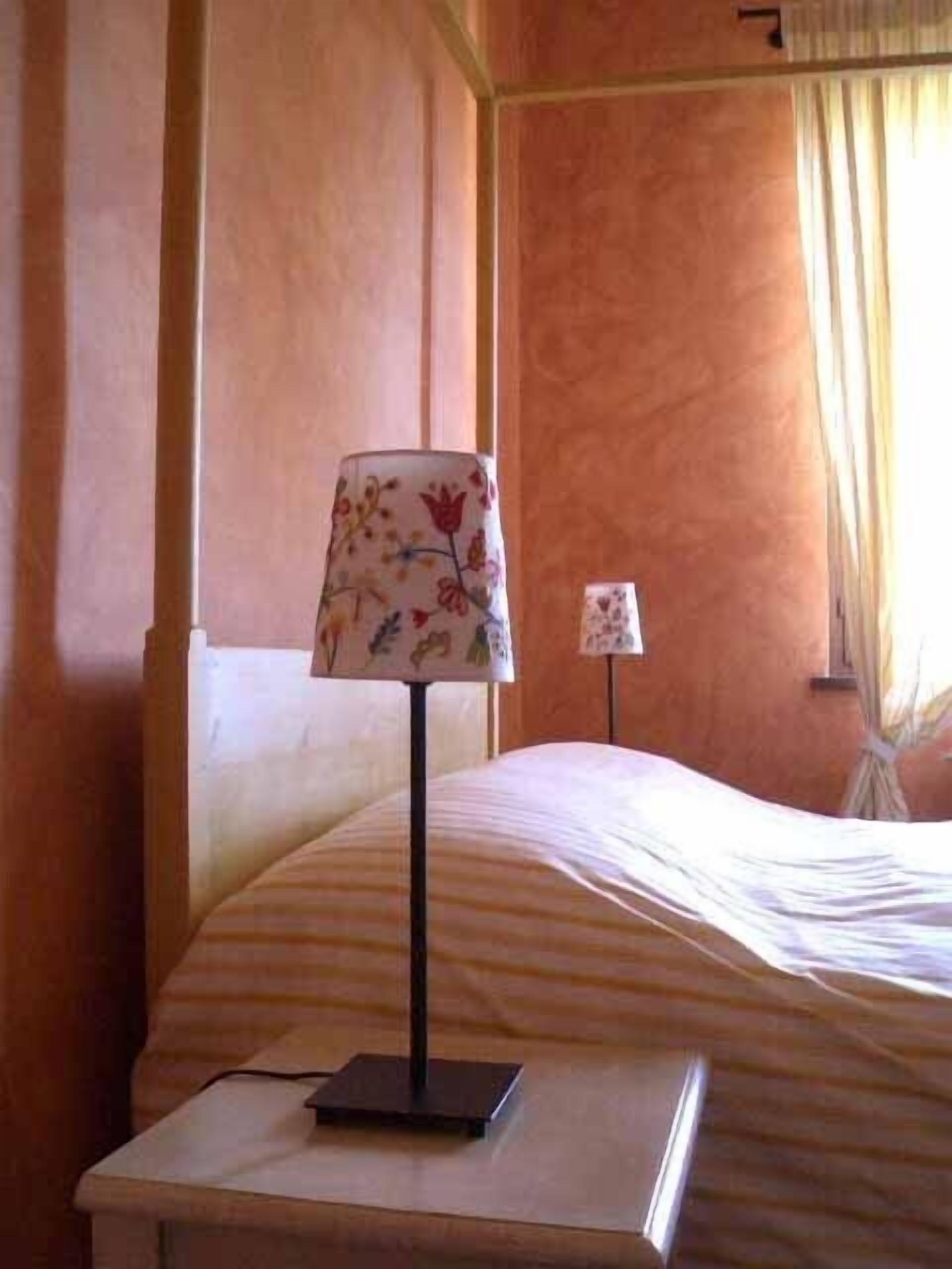 Een net opgemaakt bed met een gestreept dekbedovertrek, een nachtkastje met een lamp en een raam met gordijnen.