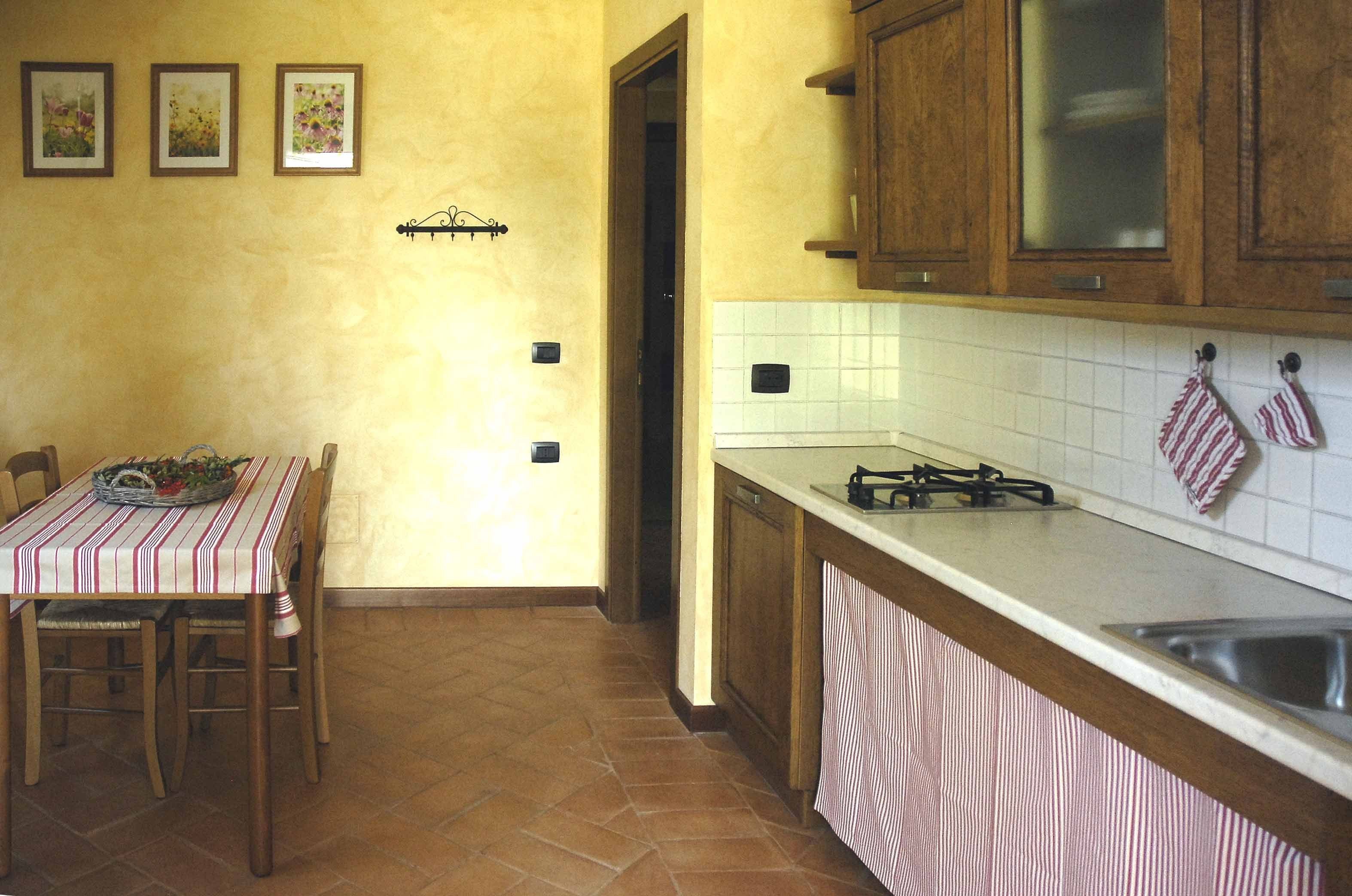 Una cocina con armarios de madera, salpicadero de azulejos, estufa y un comedor con mesa y sillas.