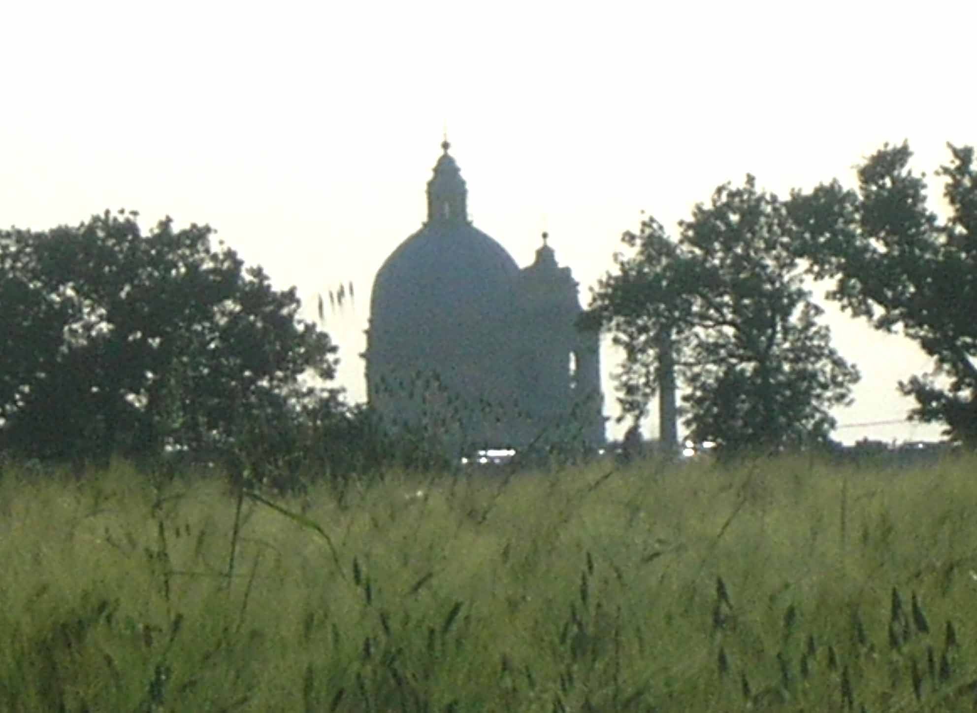 Ein großes Gebäude mit einer markanten Kuppel und einem daran angefügten kleineren Bauwerk, umgeben von Bäumen und Gras.
