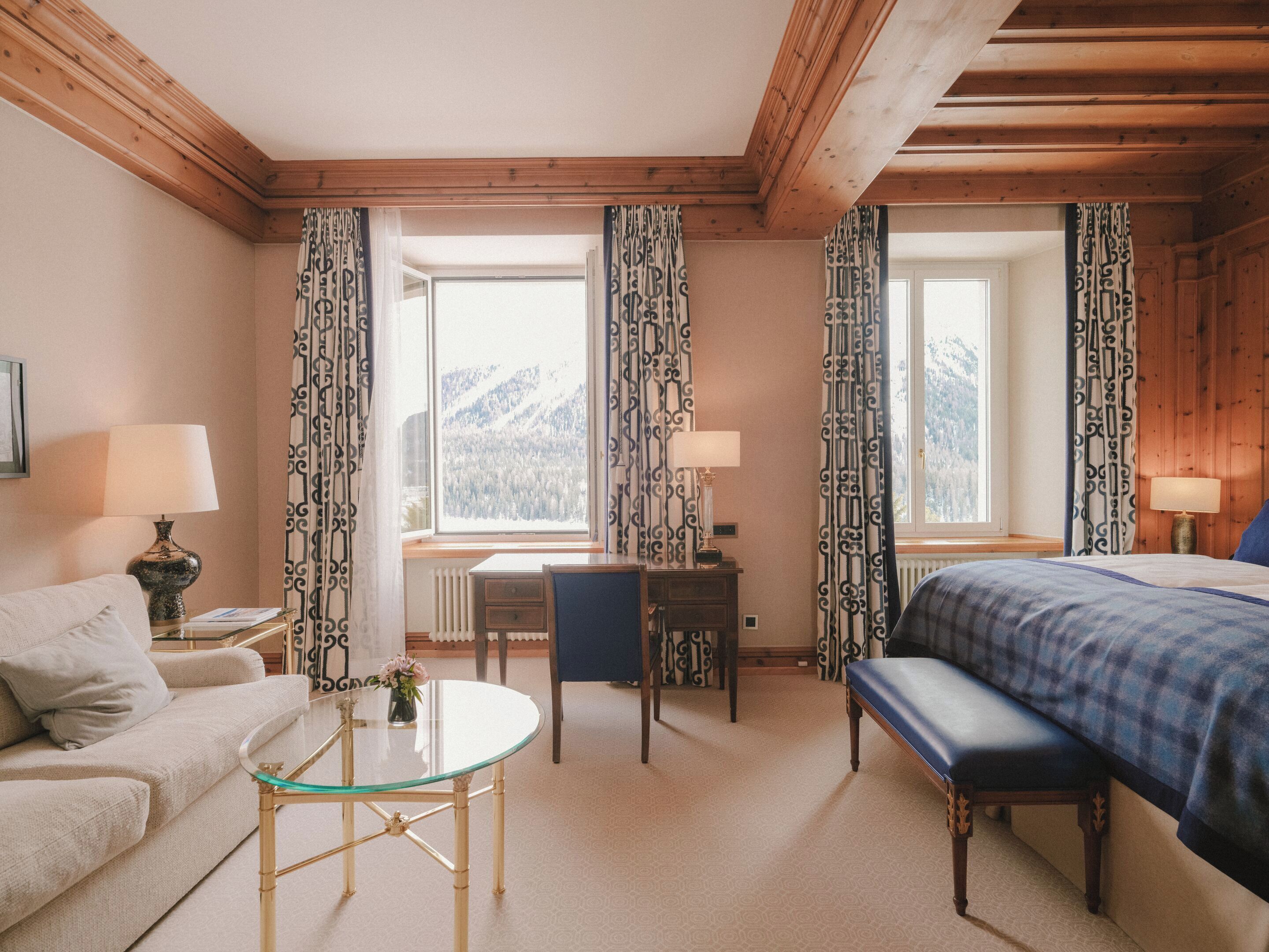 A hotel room with a bed, a sofa, a small table, a desk, and a window with curtains.