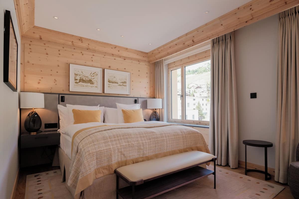 A modern bedroom with a large bed, bedside tables, a bench, and a window with curtains.