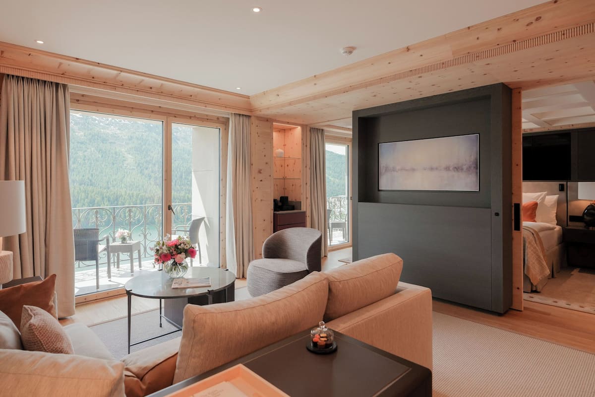 A modern hotel room with a large balcony, a flat-screen TV, and a cozy seating area.