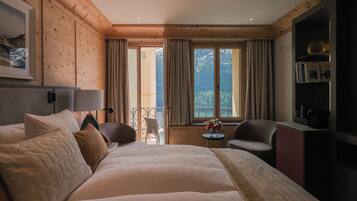 Ein Hotelzimmer mit einem großen Bett, einem kleinen Tisch mit einer Vase und Bergblick durch das Fenster.