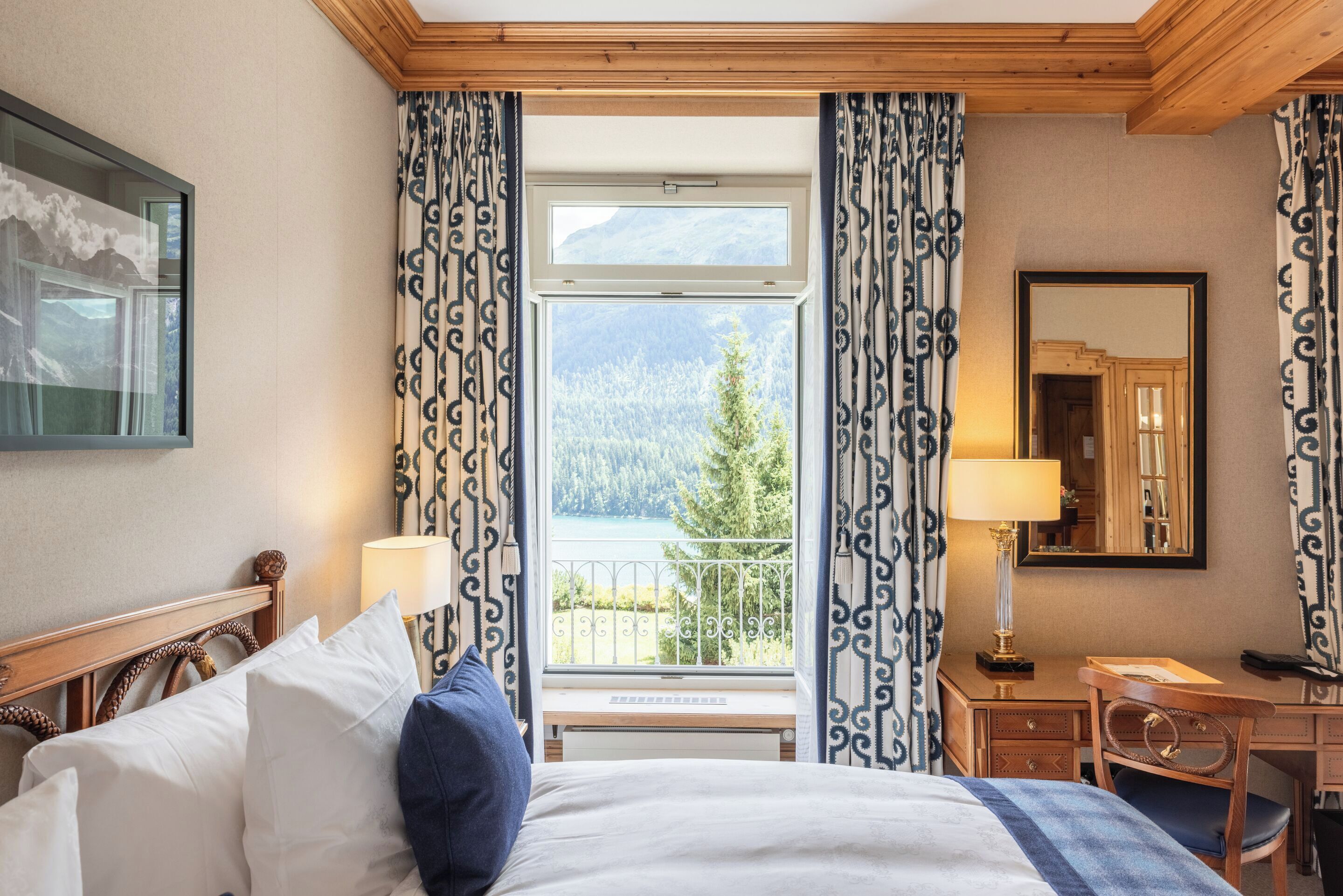 A hotel room with a bed, a desk, a chair, and a large window with curtains.