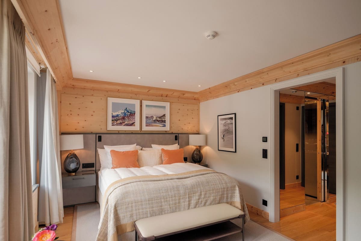 A modern hotel room with a large bed, wooden panel walls, and a view of the elevator.