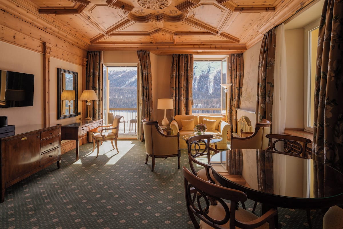 A room with a wooden ceiling, a sofa, chairs, a dining table, and a TV.
