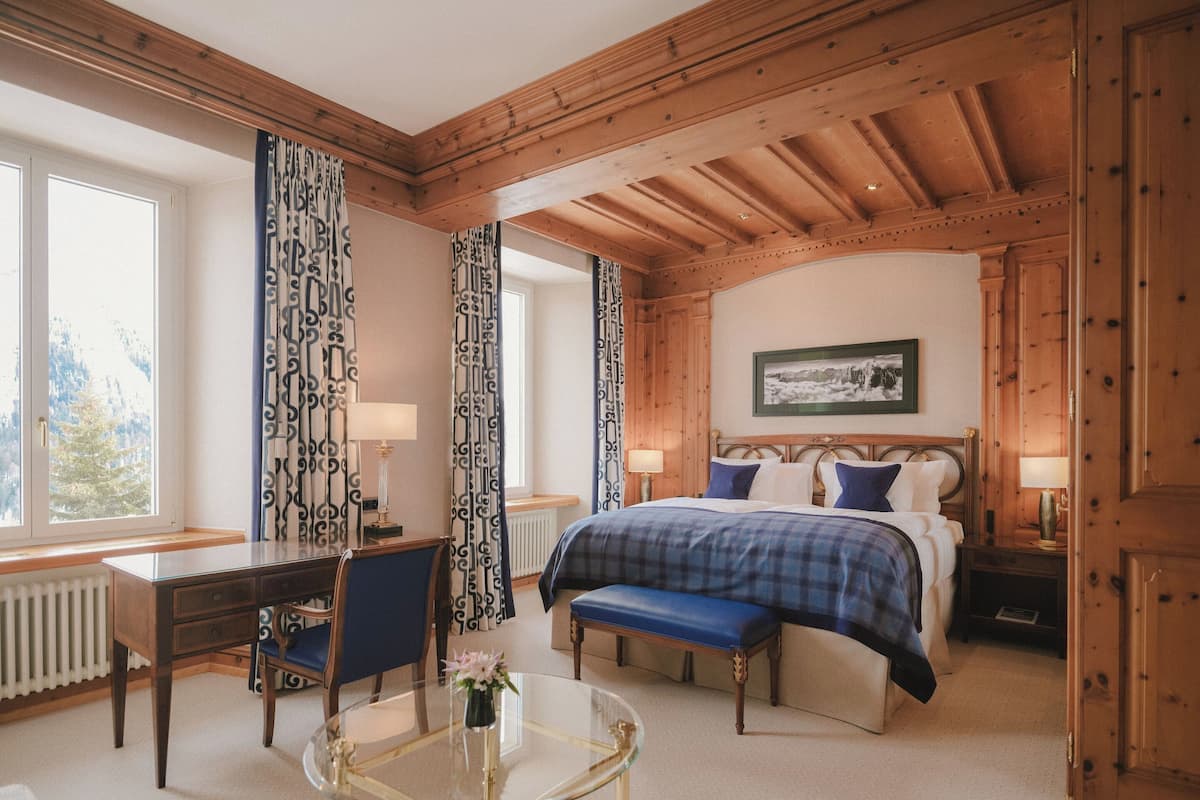 A bedroom with a bed, bedside tables, a desk, a chair, and a glass table with a vase.