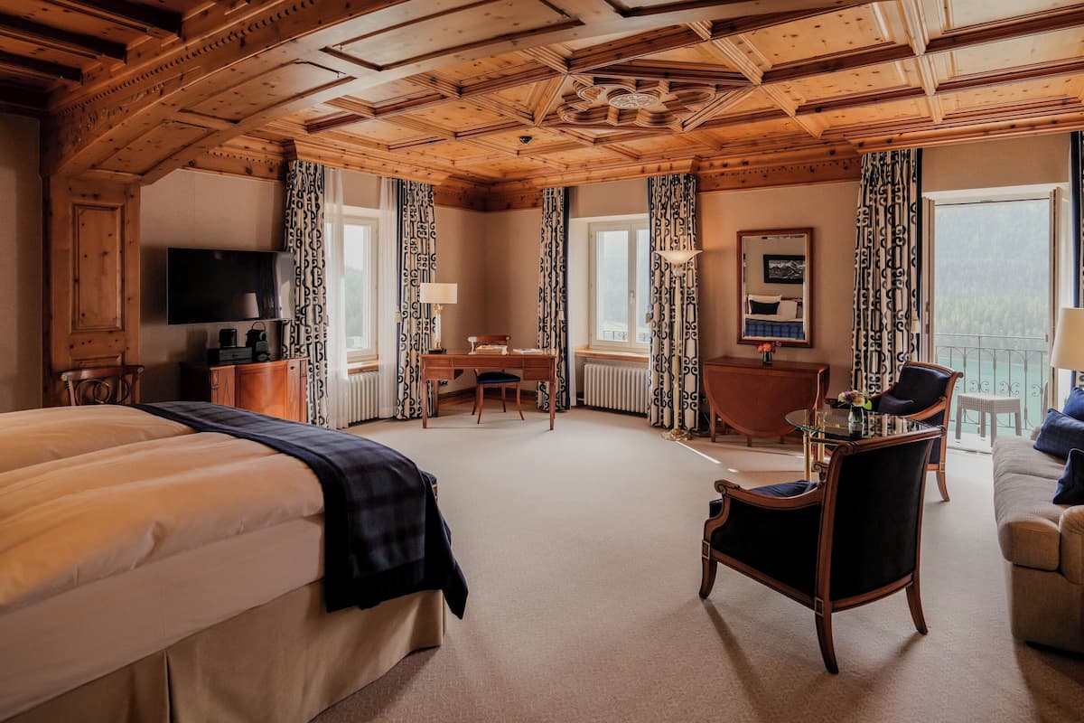 A hotel room with a large bed, a desk, a chair, and a balcony with a view.