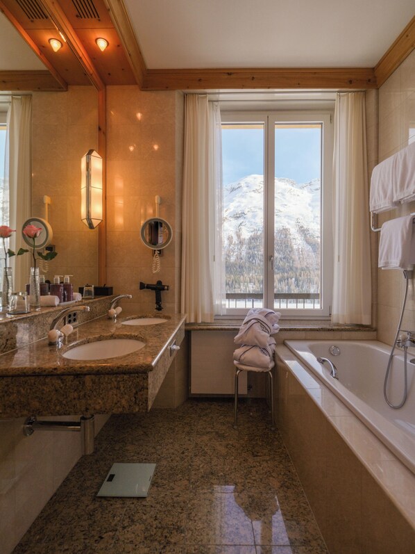 A bathroom with two sinks, a bathtub, and a window with a snowy mountain view.