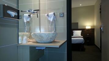 A bathroom with a large, textured bowl sink, two white hand dryers, and a mirror.