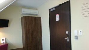 Una habitación con un armario de madera, un escritorio con silla, un televisor montado en la pared y una puerta con cerradura y panel de control.