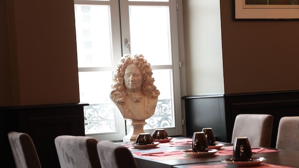 Una mesa de comedor dispuesta con platos, vasos y una escultura de busto al fondo.