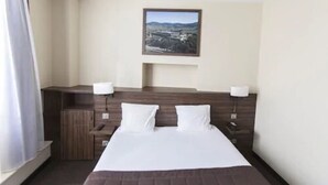 Habitación de hotel con una cama grande, una mesita de noche con lámpara, un escritorio pequeño y un cuadro colgado en la pared.
