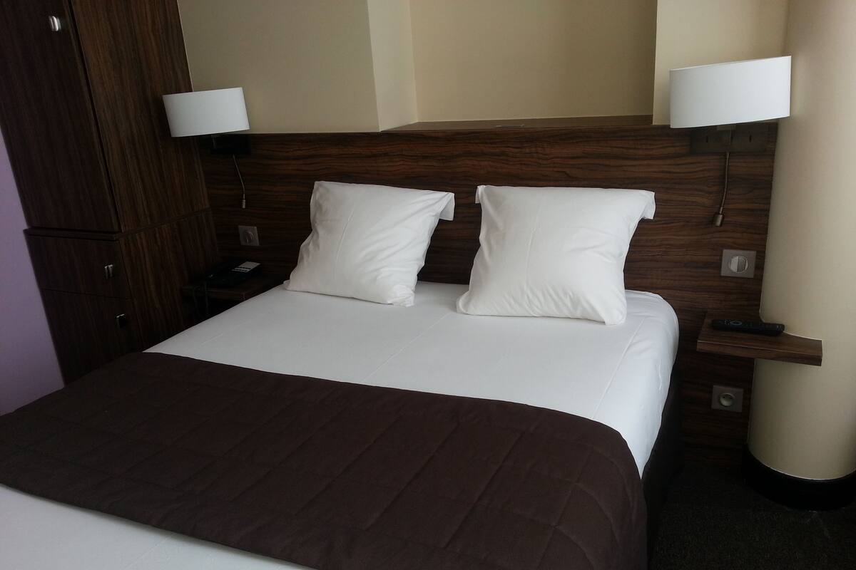 A neatly made bed with a brown bedspread and two white pillows, a wooden headboard, and two bedside lamps.