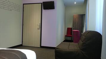 Una habitación de hotel con una cama, una silla roja, un sofá marrón, un televisor en la pared y una puerta.