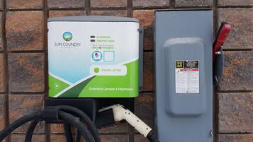 A solar-powered charging station with a green and white design, labeled "Sun Country Highway," and a grey electrical box with a red handle.
