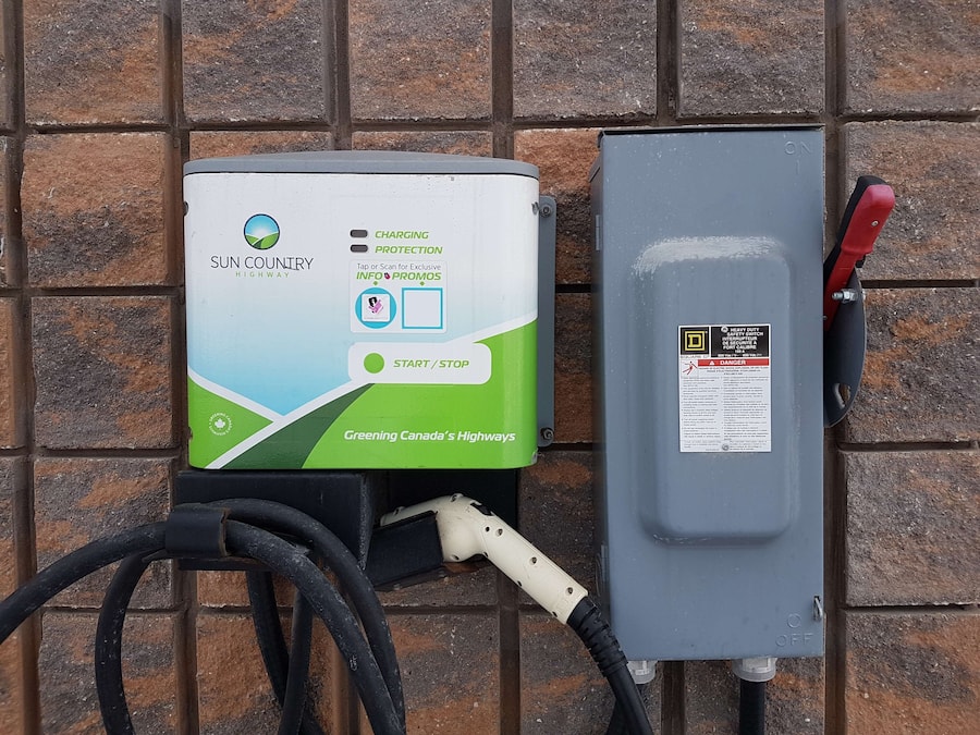 A solar-powered charging station with a green and white design, labeled "Sun Country Highway," and a grey electrical box with a red handle.