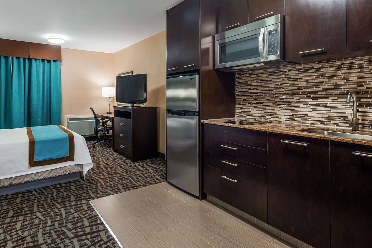 A hotel room with a bed, a desk, a television, a refrigerator, and a microwave.