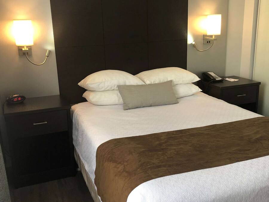 A hotel room with a large bed, two bedside tables, a nightstand, and wall-mounted lamps.