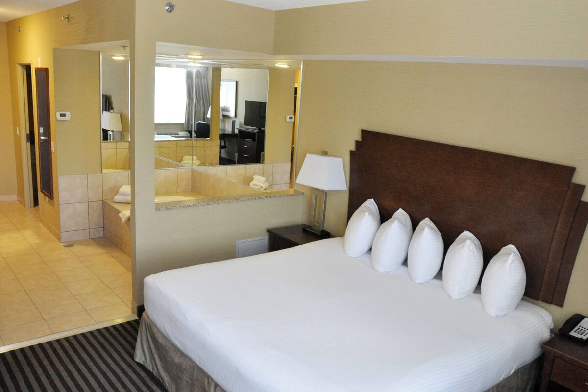 A hotel room with a large bed, a bedside table with a lamp, a mirror, and a bathroom visible through an open door.
