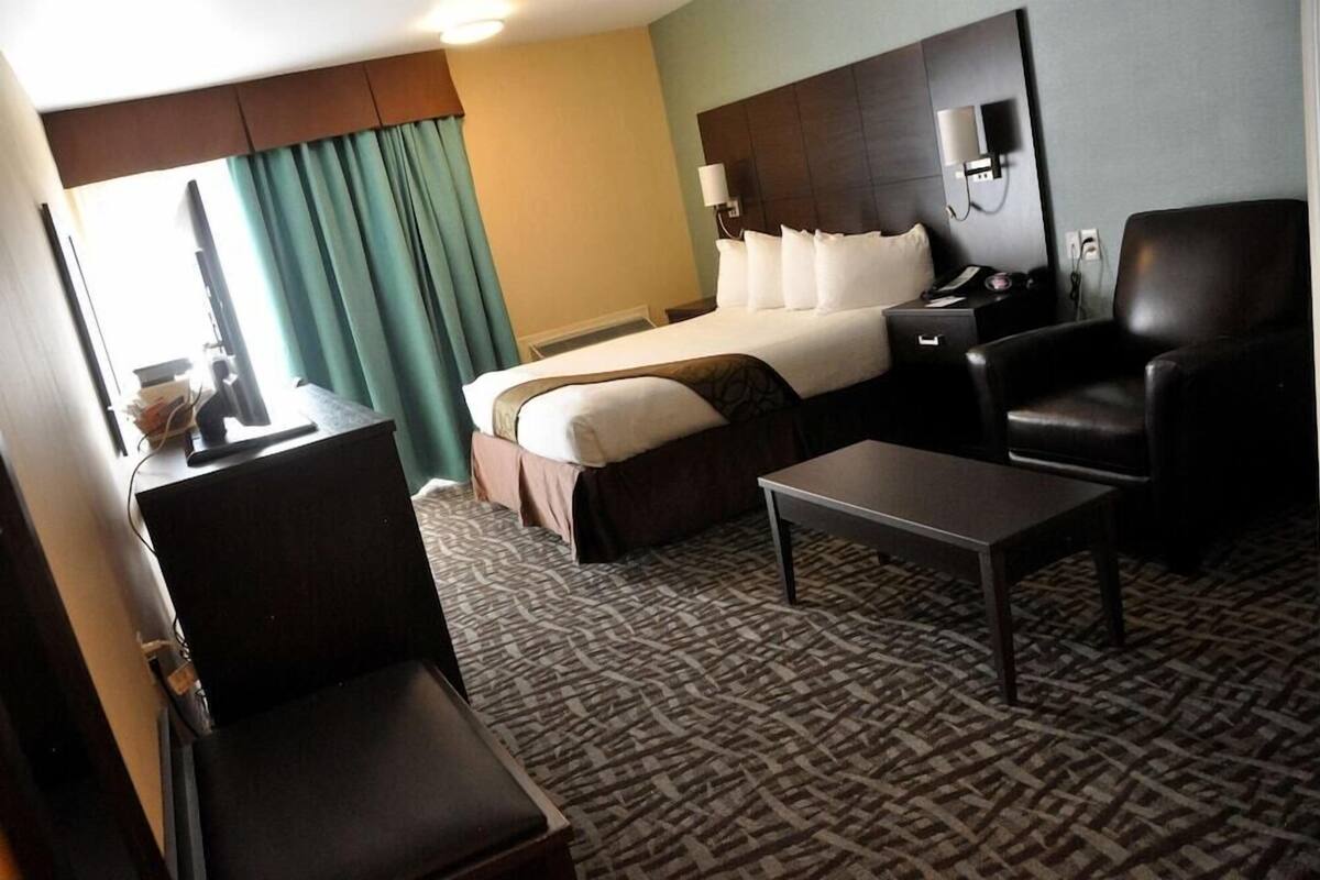 A hotel room with a bed, a desk with a computer, a chair, a table, and a large window with curtains.