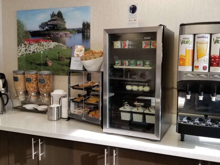 A breakfast bar with a coffee machine, a refrigerated display case with beverages, and a painting of a scenic landscape.