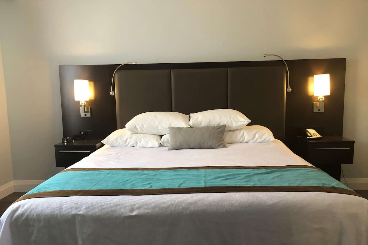A hotel room with a large bed, two bedside tables, a nightstand, and two wall-mounted lamps.