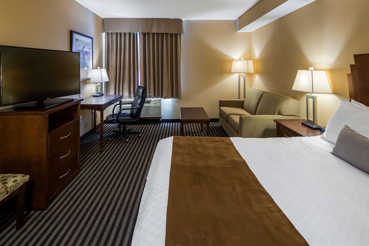 A hotel room with a bed, a desk, a chair, a TV, and two lamps.