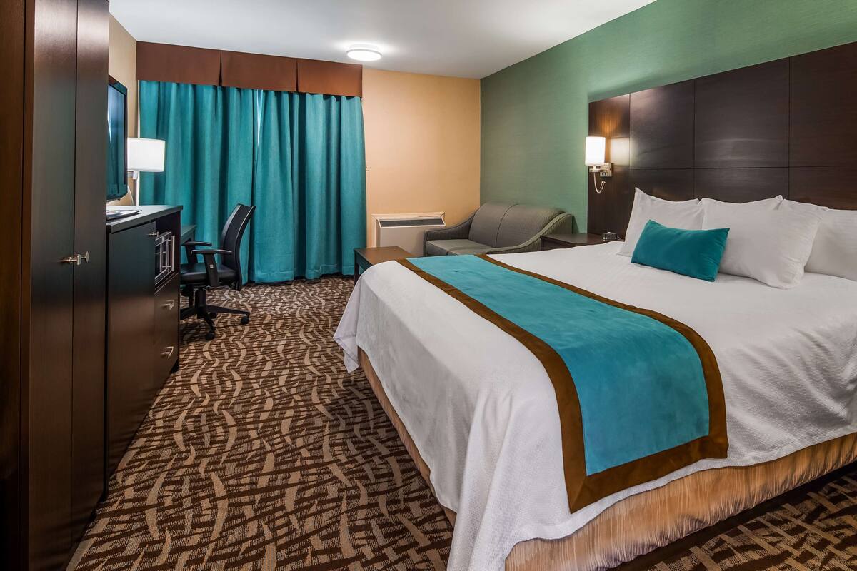 A hotel room with a large bed, a desk, a chair, and a wardrobe.