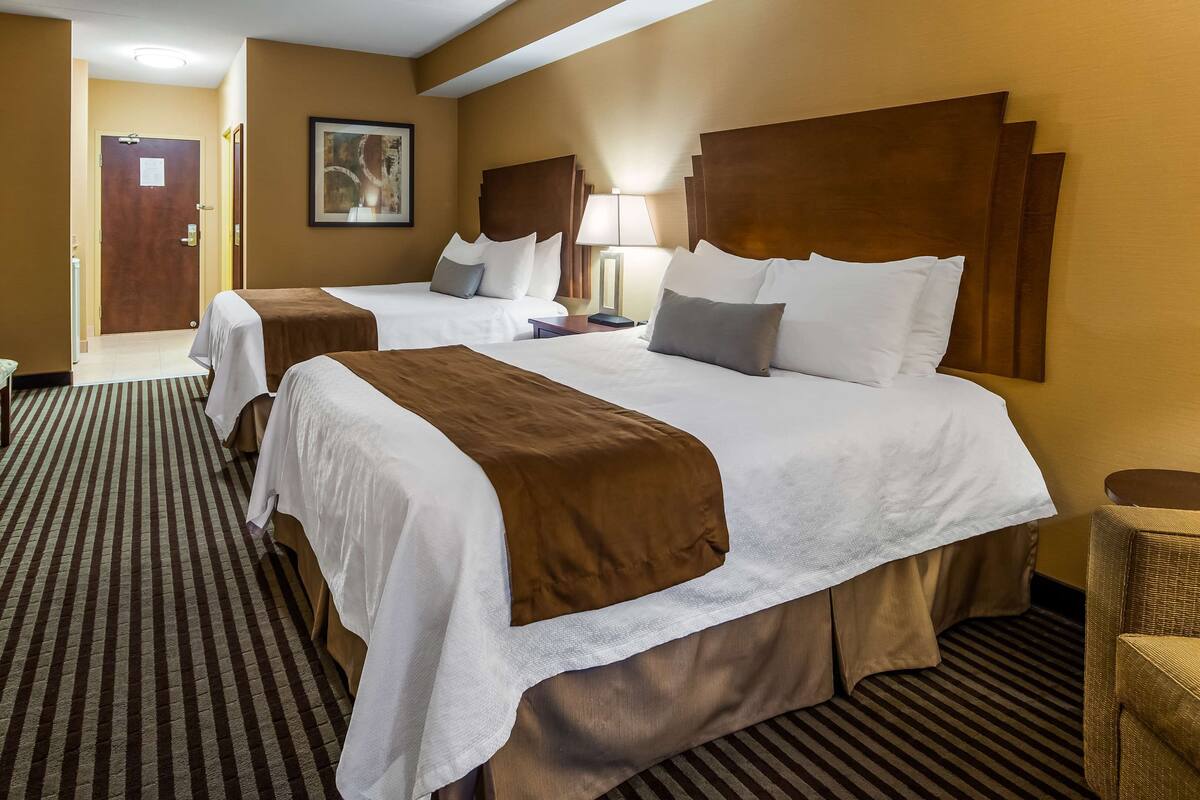 A hotel room with two beds, a TV, a desk, and a chair.