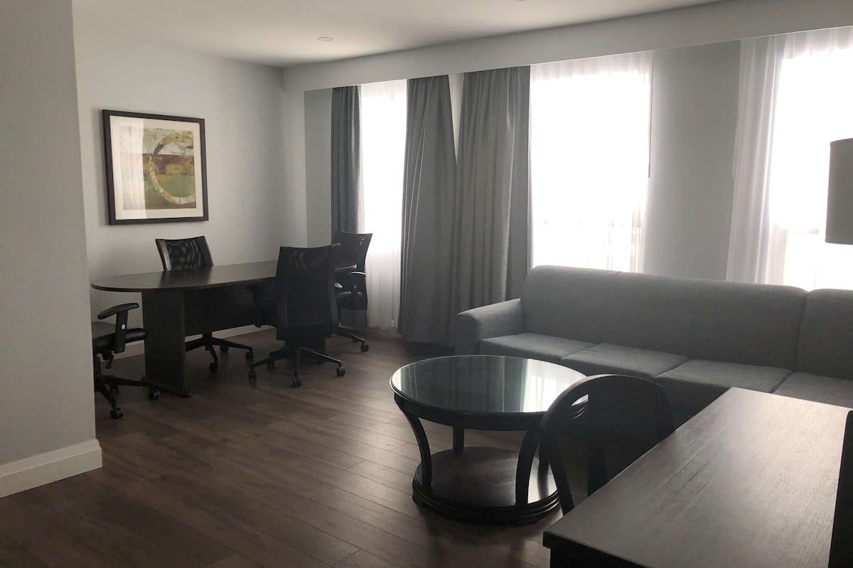 A modern living room with a sofa, a glass coffee table, a desk with a chair, and a framed picture on the wall.