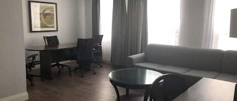 Una sala de estar moderna con un sofá, una mesa de centro de vidrio, un escritorio con una silla y un cuadro en la pared.