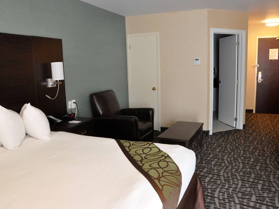 A hotel room with a bed, a desk, a chair, a nightstand, a lamp, and a door leading to another room.