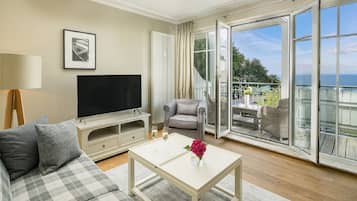 Una sala de estar con sofá, una mesa de centro con una flor, televisor y balcón con vistas.