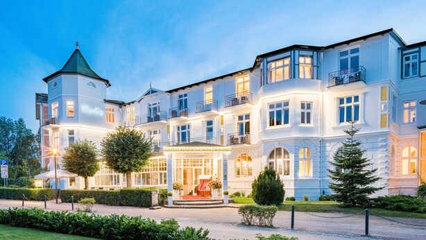A large, multi-story hotel with a prominent tower, a well-lit entrance, and a manicured garden. - Hotel Residenz Waldkrone (Kuehlungsborn)