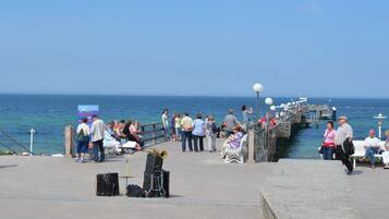 A pier with people walking and sitting, a musician with a trumpet, and a clear view of the sea.