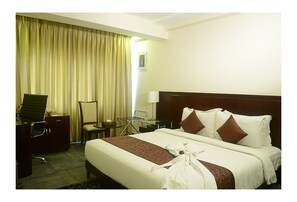 Une chambre d’hôtel avec un grand lit, un bureau avec une chaise, une lampe et une fenêtre avec des rideaux.